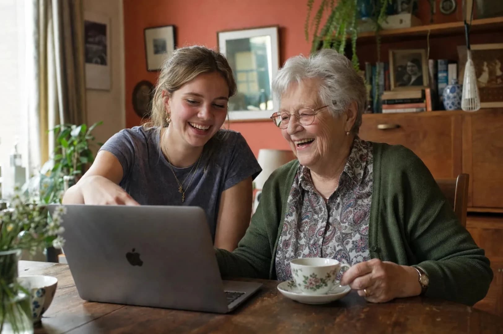 A student and an older homeowner laughing together over a laptop at the kitchen table